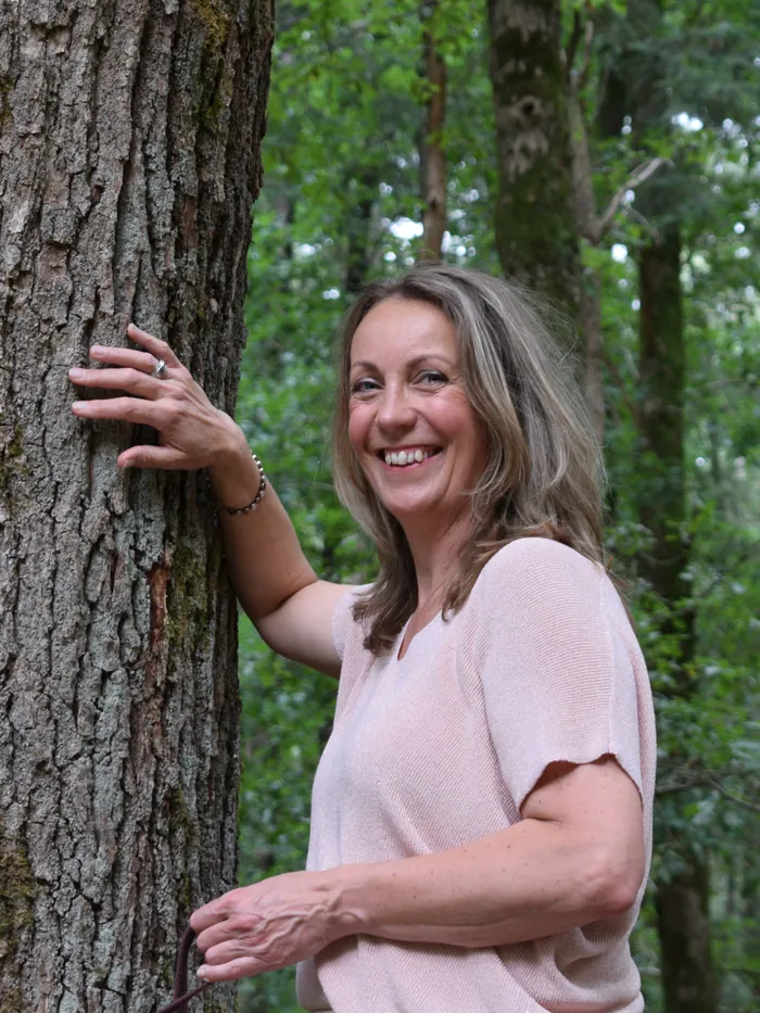Marjon Brinks lacht, met haar hand tegen een boomstam in het bos