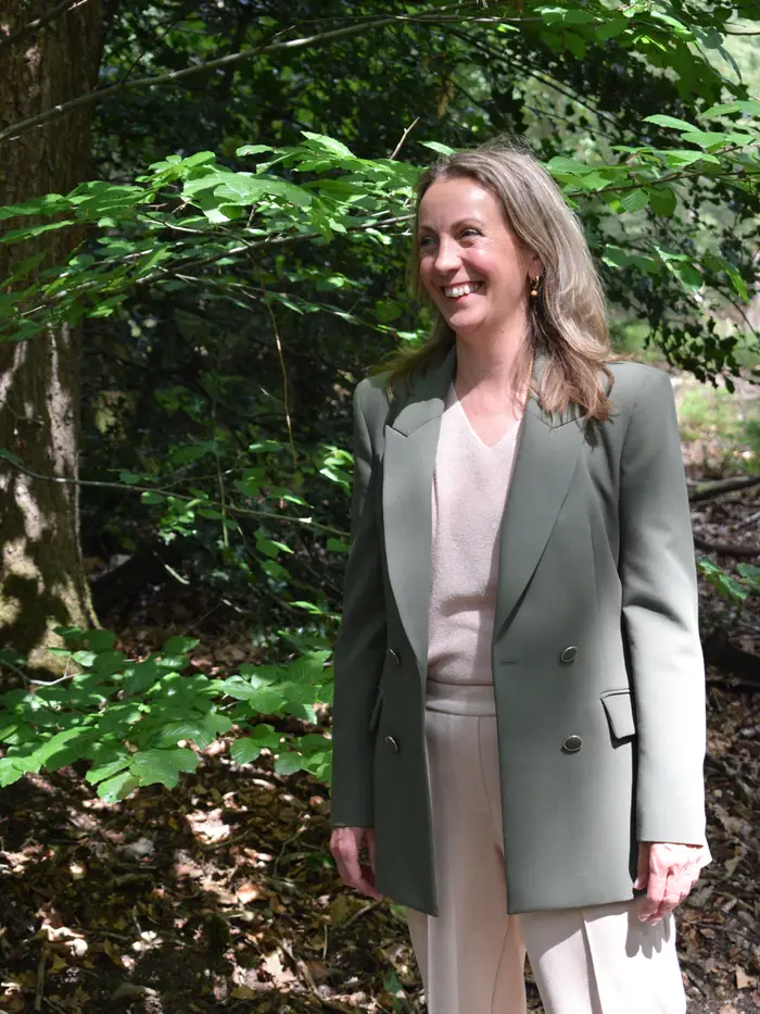 Marjon Brinks staat ontspannen in het bos en kijkt lachend opzij