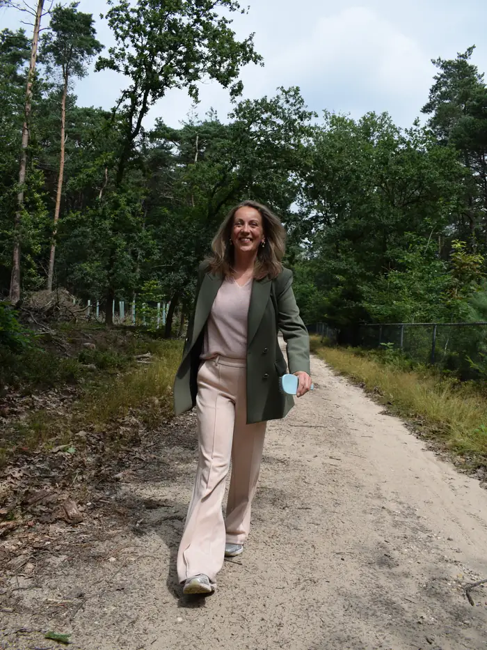 Marjon Brinks wandelt lachend over een zandpad door het bos