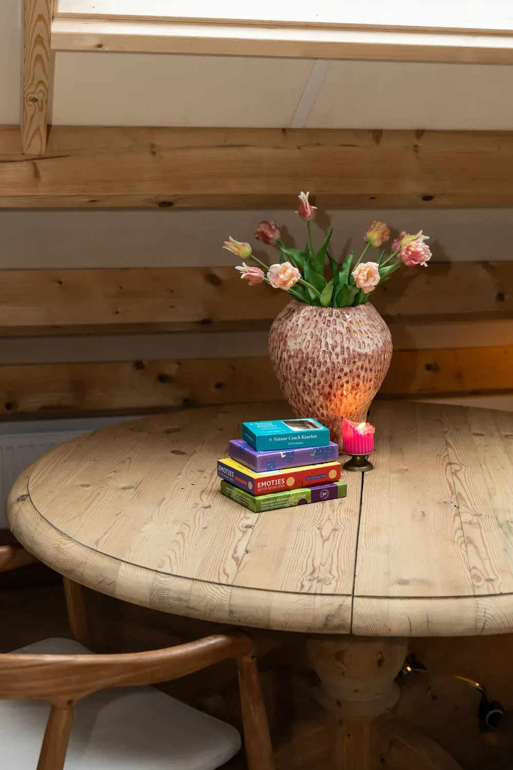 Stapel coachkaarten met een kaars en een vaas tulpen op de ronde tafel in de praktijk