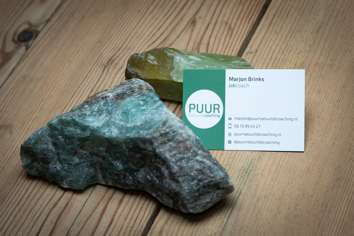Het visitekaartje van Marjon Brinks, jobcoach, naast twee ruwe groene edelstenen op een houten tafel