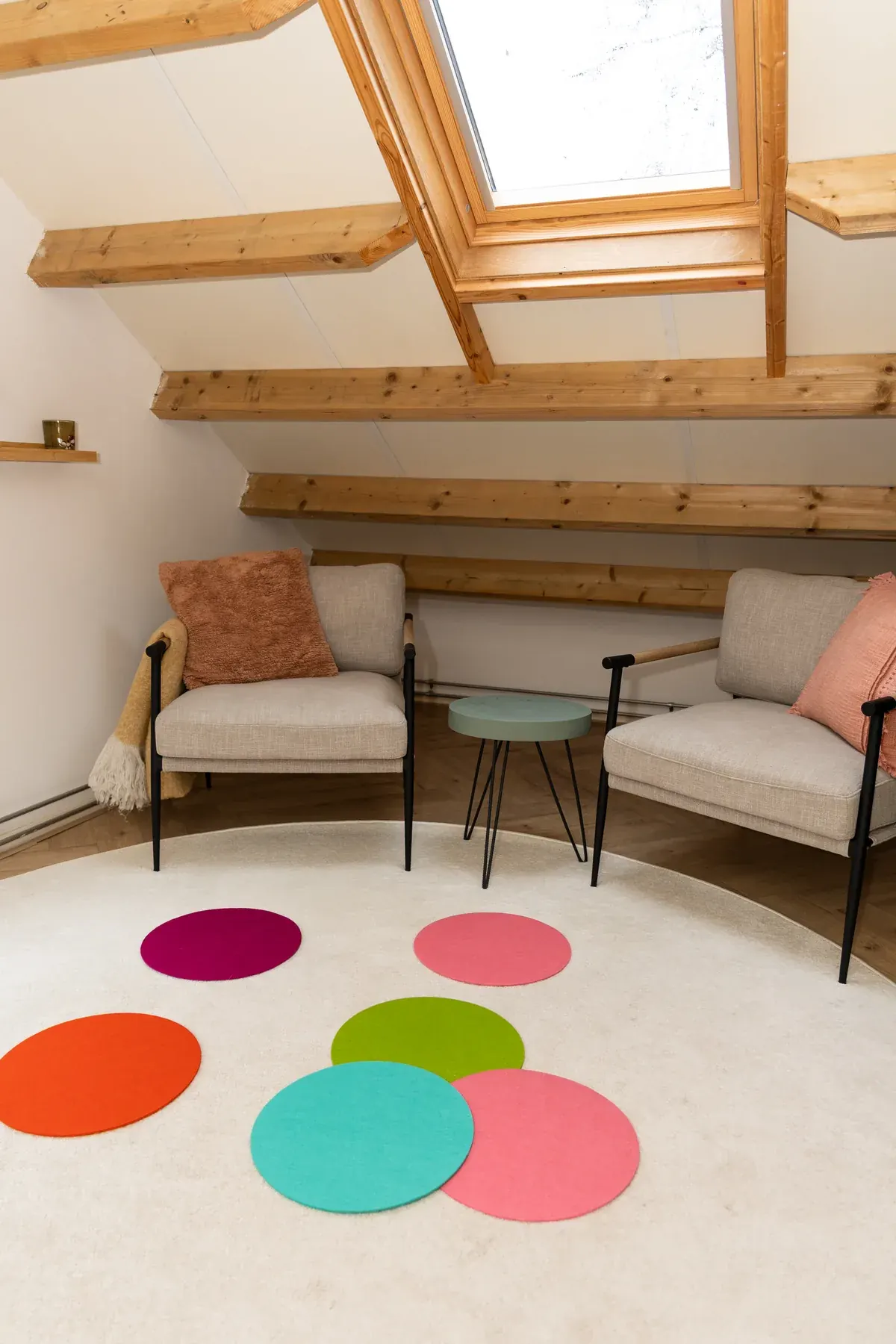 De praktijkruimte met gekleurde vilten cirkels op het ronde vloerkleed, twee stoelen en een dakraam
