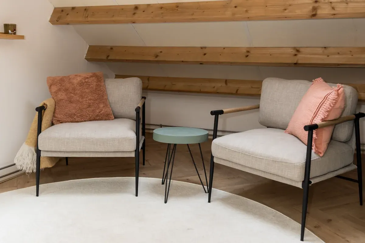 De zithoek: twee fauteuils met een bijzettafel onder houten balken